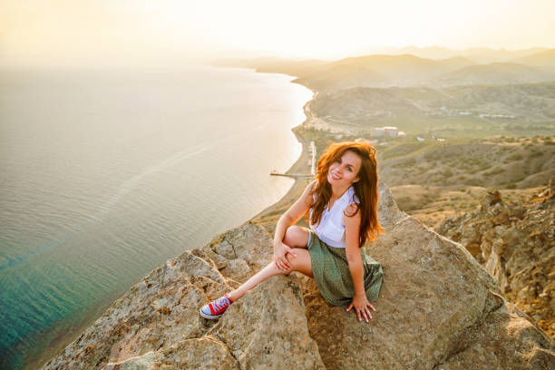 photo panoramique d’une femme heureuse aux mains ouvertes qui a conquis le sommet d’une falaise avec une belle vue sur la mer et le paysage urbain. le concept de voyage et de liberté. - conquered photos et images de collection