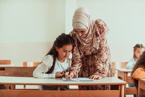 Female hijab Muslim teacher helps school kids to finish their lesson. Selective focus.High quality photo