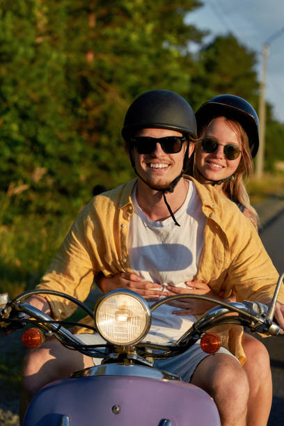 istock Happy young couple smiling at camera while riding a scooter and having fun at sunset 1340297413