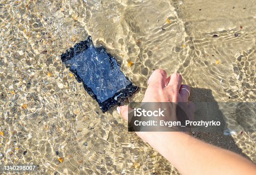 istock A woman's hand lifts a her smartphone from sea water on the beach. 1340298007
