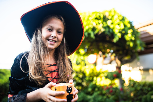 A pretty girl in a witch costume is holding a bowl of Halloween candy