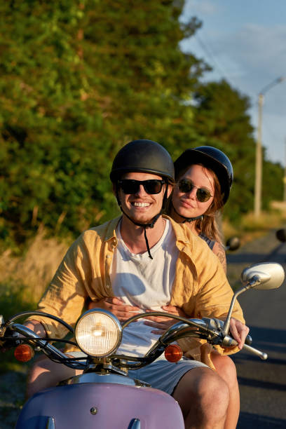 jeune couple joyeux souriant à la caméra tout en conduisant un scooter rétro et en s’amusant en dehors de la ville - motorcycle motor scooter couple young adult photos et images de collection