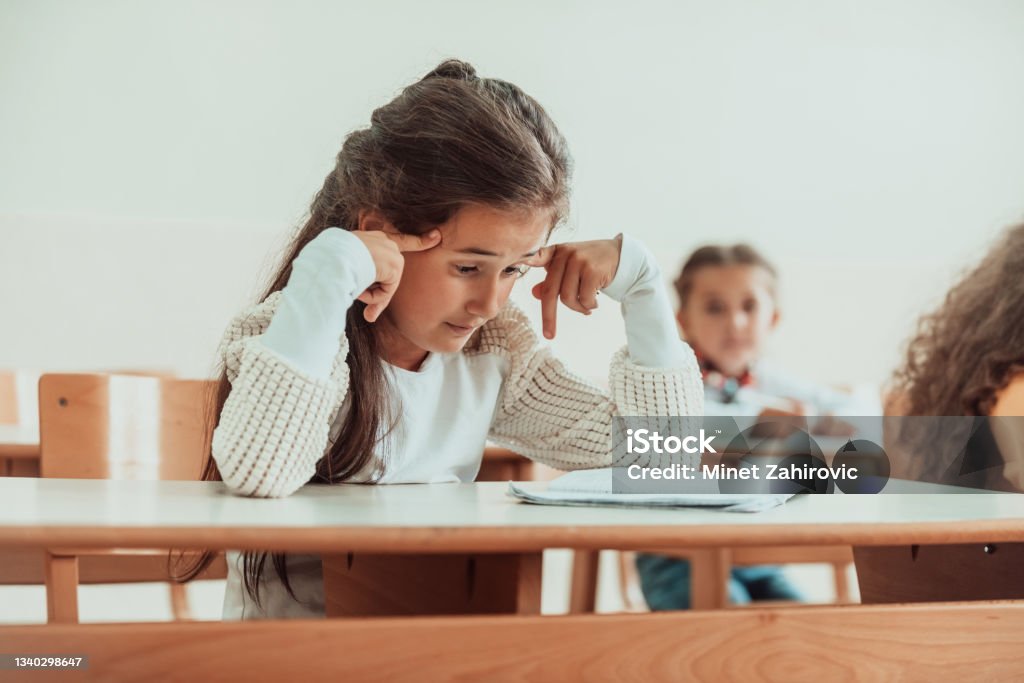 The girl sitting confusedly with her hands on her head in the school desk and attends classes. Selective focus The girl sitting confusedly with her hands on her head in the school desk and attends classes. Selective focus . High quality photo Anxiety Stock Photo