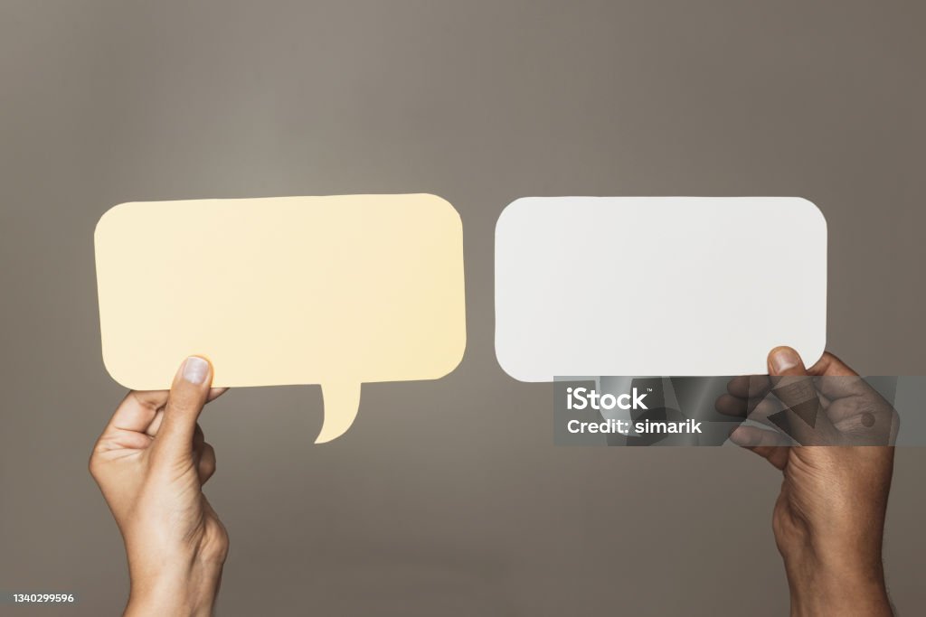 Speech Bubbles Two hands are holding two speech bubbles which are white and yellow in front of brown background. Simplicity Stock Photo