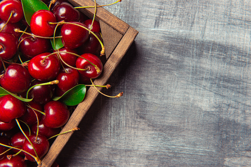 Fresh cherries in a wood container, gray background.