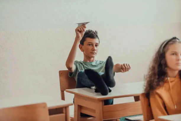 A naughty boy with his feet on a desk sits in the classroom and throws a plane. Selective focus . High quality photo