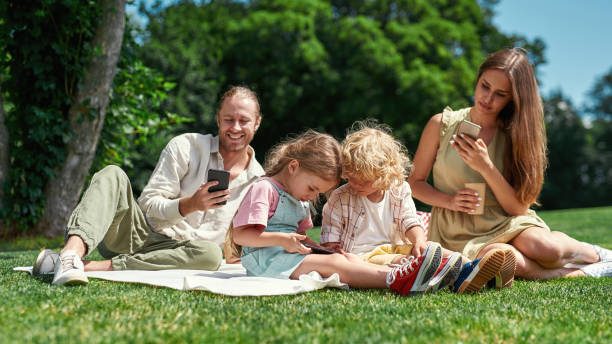istock Busy family spending time together outdoors, using smartphone while having picnic in nature on a summer day 1340300231