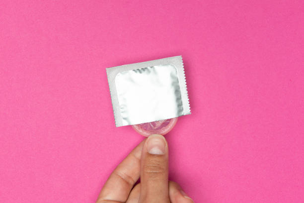 Woman Holding a Condom Hand holding a condom, pink background. condom photos stock pictures, royalty-free photos & images