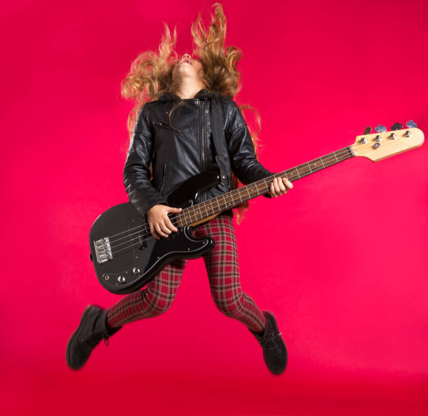 Blond Rock and roll girl with bass guitar jump on red Blond Rock and roll girl jumping playing bass guitar on red background bass guitar photos stock pictures, royalty-free photos & images