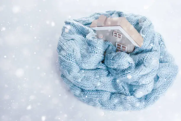 Photo of toy wooden house wrapped in a warm knitted scarf on a white background