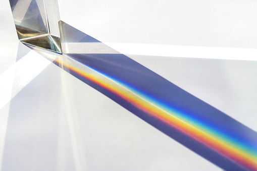 Glass prism for optical physics experiments in education, splitting the light into reflection beams in the spectrum of rainbow colors, bright background, copy space, selected focus