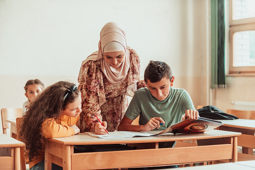 Female hijab muslim teacher helps school kids to finish they lesson. Selective focus .High quality photo