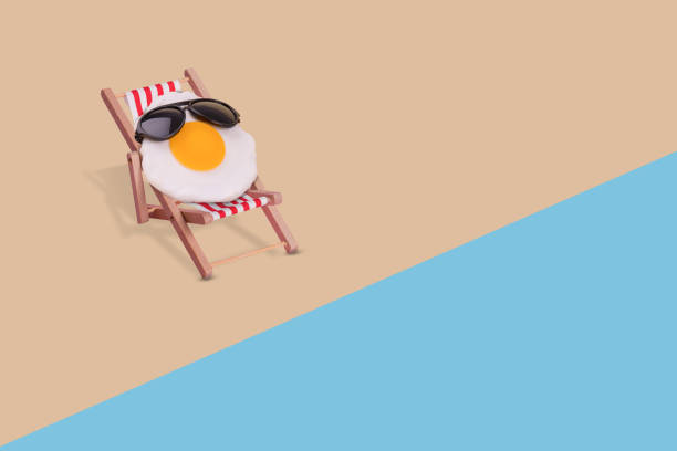 istock Creative funny composition made of fried egg with sunglasses sitting on deck chair on the beach. 1340308240