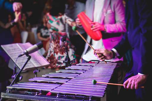 Xylophone concert view of vibraphone marimba player, mallets drum sticks, with a latin orchestra musical band performing in the background