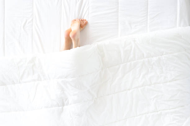 Women legs stick out from under covers in bed. Sleep problems and insomnia concept