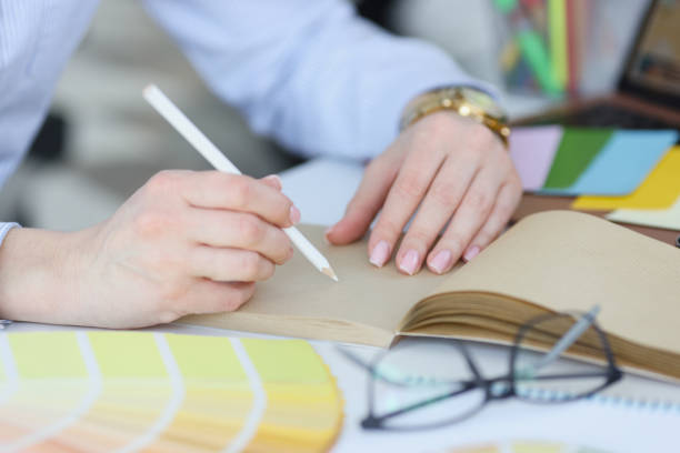 istock Woman holds in hand white pencil and notebook on desktop closeup 1340313087