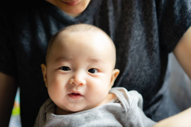 Asian cute happy baby smiling and sitting on mom. use as concept of mood, health, baby development. stock photo