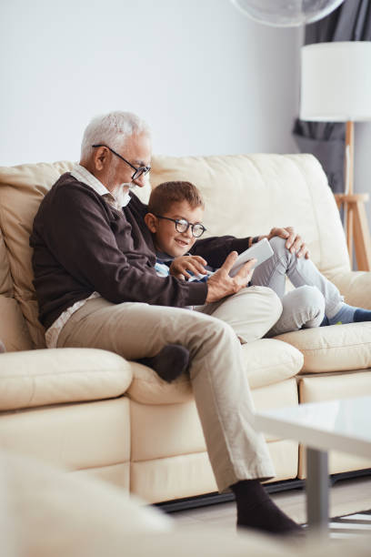 istock Happy grandfather and grandson watching something on digital tablet while relaxing on the sofa. 1340320148