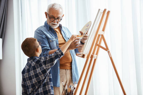 istock Grandfather and grandson talking while painting on canvas at home studio. 1340320460