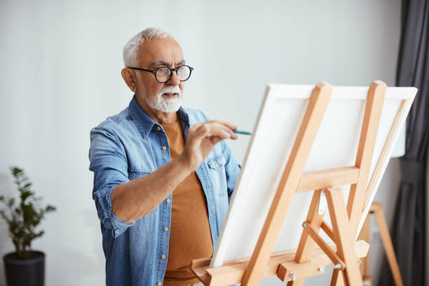 artista senior che dipinge su tela nel suo studio di casa. - painting foto e immagini stock