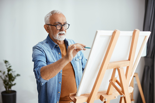 Mature man creating a new painting on canvas at home.