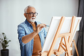 Senior artist painting on canvas at his home studio.