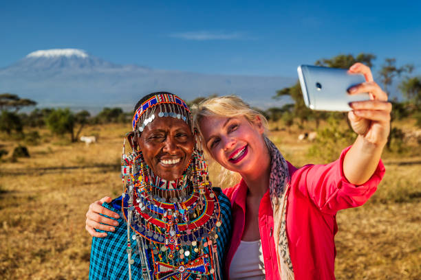 Young woman taking selfie with Maasai woman, Mount Kilimanjaro on background, Kenya, Africa stock photo