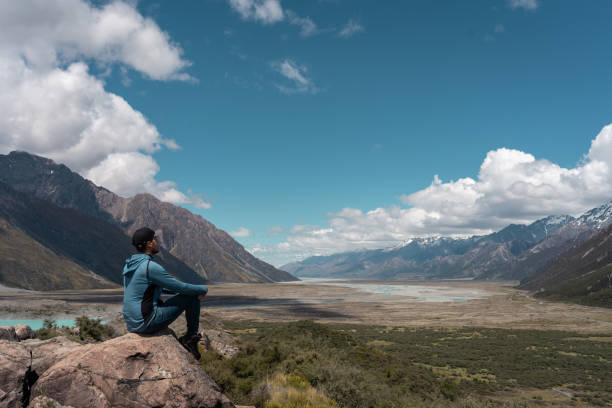 istock Man sitting on a rock looking at the amazing view of the valley in Mount Cook National park 1340347311
