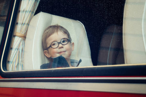 A little boy with round eyeglasses looks through the long distance bus window (vintage tinting processing, noises, film photo) stock photo