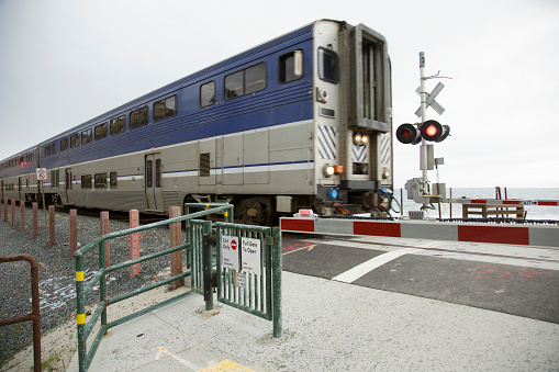 end of blue and silver passenger train finally passing rail road crossing. Red lights flashing, arm still down.