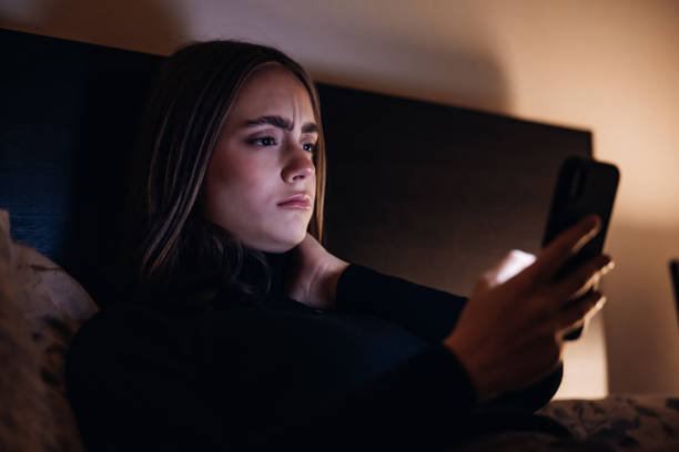悪いニュース若い女性は夜ベッドに横たわっている携帯電話でメッセージを読む - 信じられない ストックフォトと画像