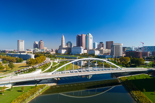 Downtown Columbus skyline aerial with a clear blue sky in the background and the Scioto River and the Main Street Bridge in the foreground.