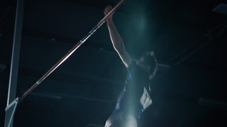 Pole Vault Jumping Championship: Professional Male Athlete Running with Pole Successfully Jumping over Bar and Landing on His Feet. Dramatic Colors, Slow Motion Close-up Shot of Sport Achievement