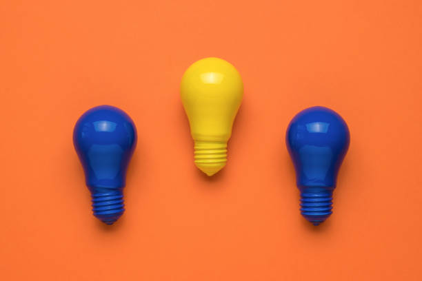 istock Two blue light bulbs and one yellow on an orange background. Minimalism. Flat lay. 1340385829