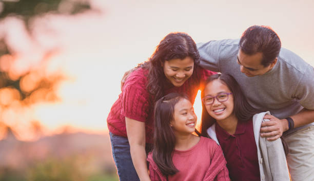 Casual Filipino family photo A Filipino family of four pose casually for a photo in the evening sun.  The two daughters are seated in front and their parents are leaning over the top and looking down at them.  They are all dress casually and smiling as they enjoy the time together. happy filipino family stock pictures, royalty-free photos & images