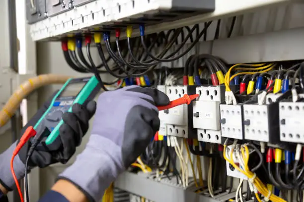 Photo of Electrician engineer tests electrical installations and wires on relay protection system. Adjustment of scheme of automation and control of electrical equipment.
