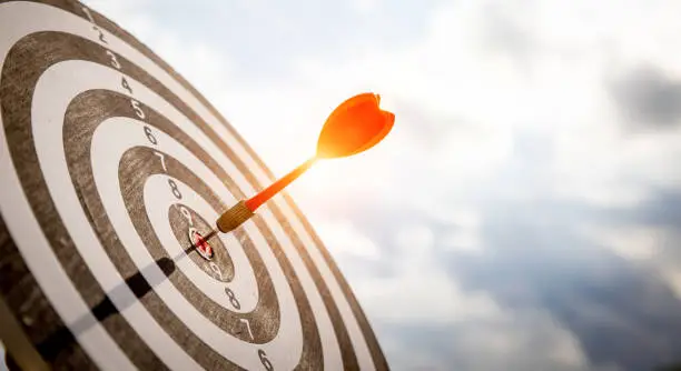 Photo of Close up shot red darts arrows in the target  of dartboard center on dark blue sky background. Business target or goal success and winner concept.