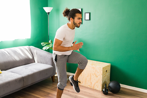 Running in place. Sporty latin man running in the living room while doing his daily cardio routine at home