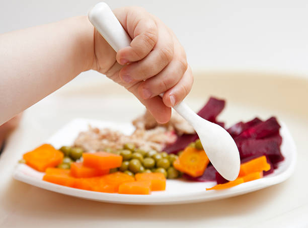 Baby's hand with a spoon and plate with vegetables 