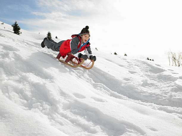 junge auf einem schlitten spielen im schnee - schlittenfahren stock-fotos und bilder