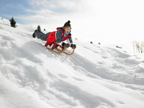 Caucasian boy and his mother sledding with sled on a small hill, during a winter day on the mountain