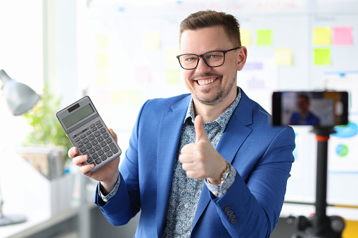 Smiling blogger businessman holds a calculator and records training videos about earnings. Profitable financial investments concept