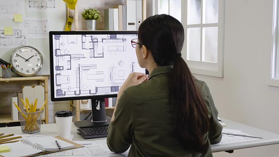 asian woman interior designer looking floor plan of new house indoor design on monitor concentrated thinking idea. Blueprint architect construction project sketch concept on laptop computer screen.