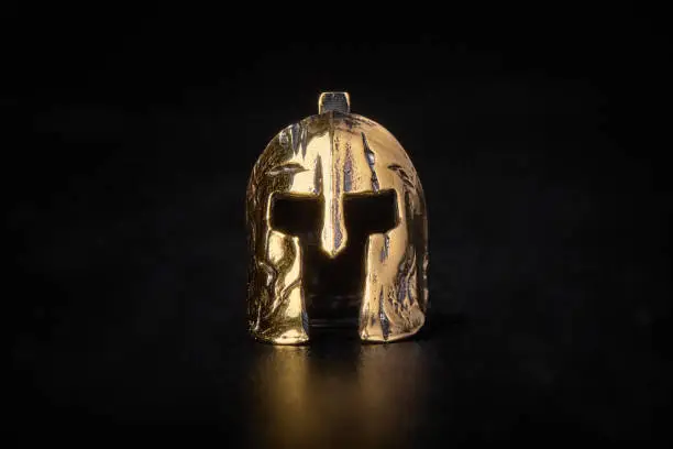 A figurine. Golden Spartan helmet. Metal on a black background. Headgear and equipment of soldiers
