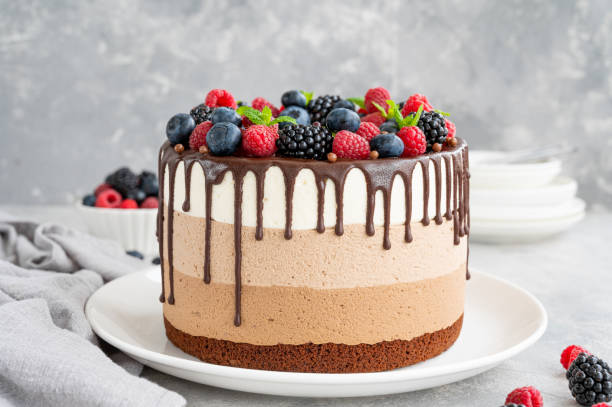 istock Three chocolate mousse cake with chocolate glaze, blueberries, raspberries and blackberries on top on a white plate on a gray concrete background. Cake with three layers of different taste. Copy space. 1340425955