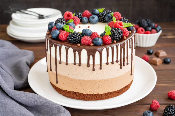 istock Three chocolate mousse cake with chocolate glaze, blueberries, raspberries and blackberries on top on a white plate on a dark wooden background. Cake with three layers of different taste. Copy space. 1340425981