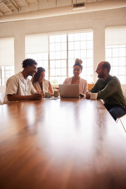 istock Laughing businesspeople working on a laptop around an office table 1340431642