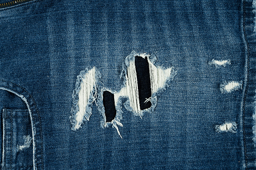 The textured design of these blue women's jeans has a tear mark on the front pocket.