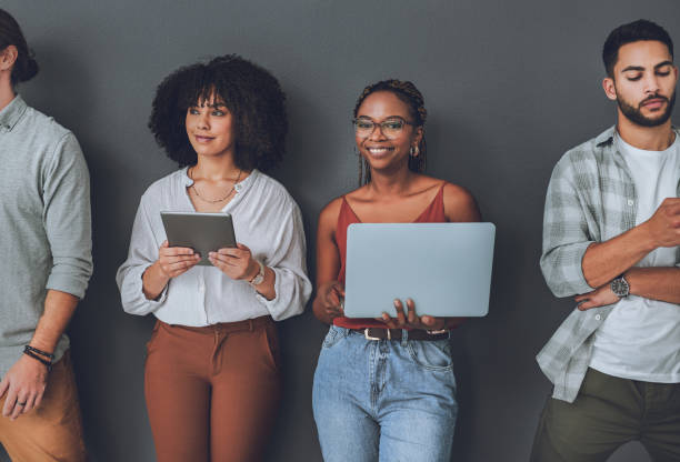 istock Studio portrait of a young woman using a laptop while standing alongside other people against a grey background 1340434815