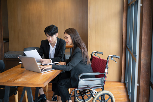Handicapped woman in wheelchair working on new business project with her colleague in office.